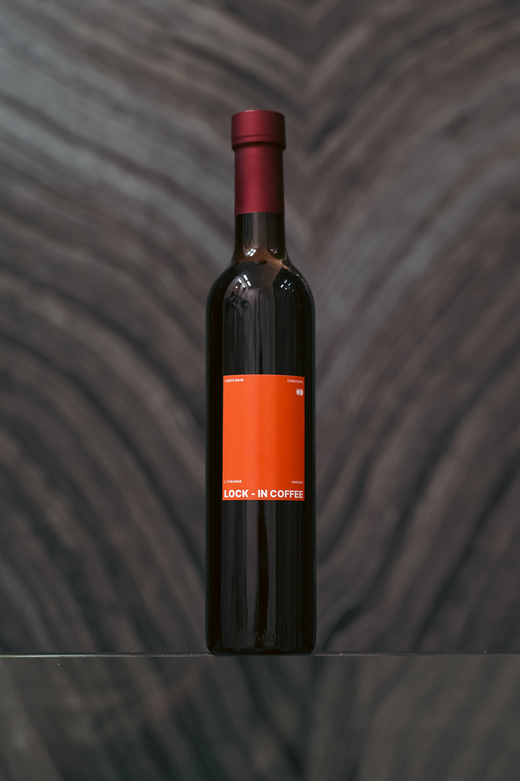 Dark glass bottle with a red cap and label on a textured gray background